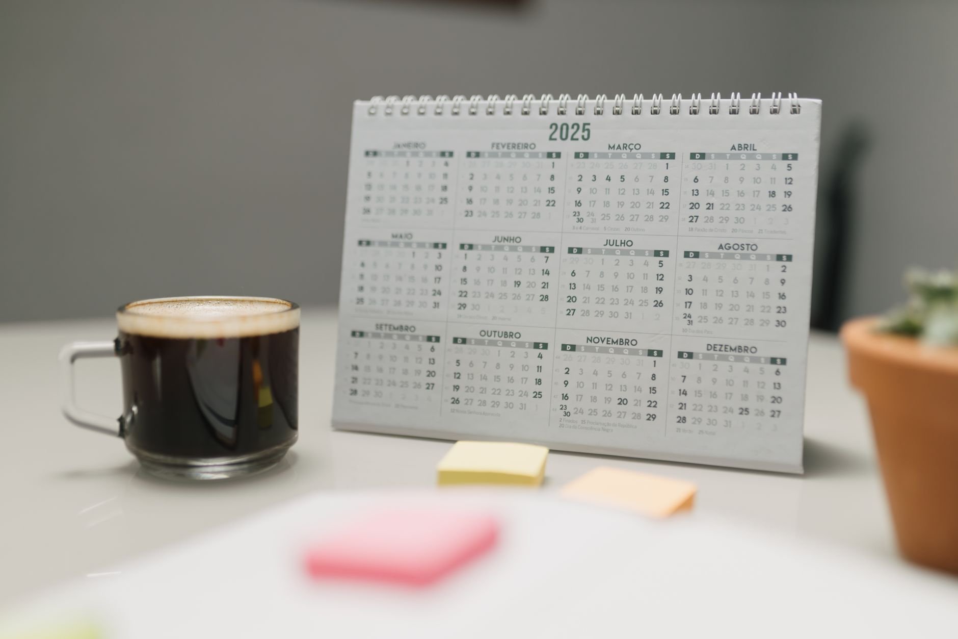A 2025 calendar on a desk with coffee, sticky notes, and a plant in an office setting.