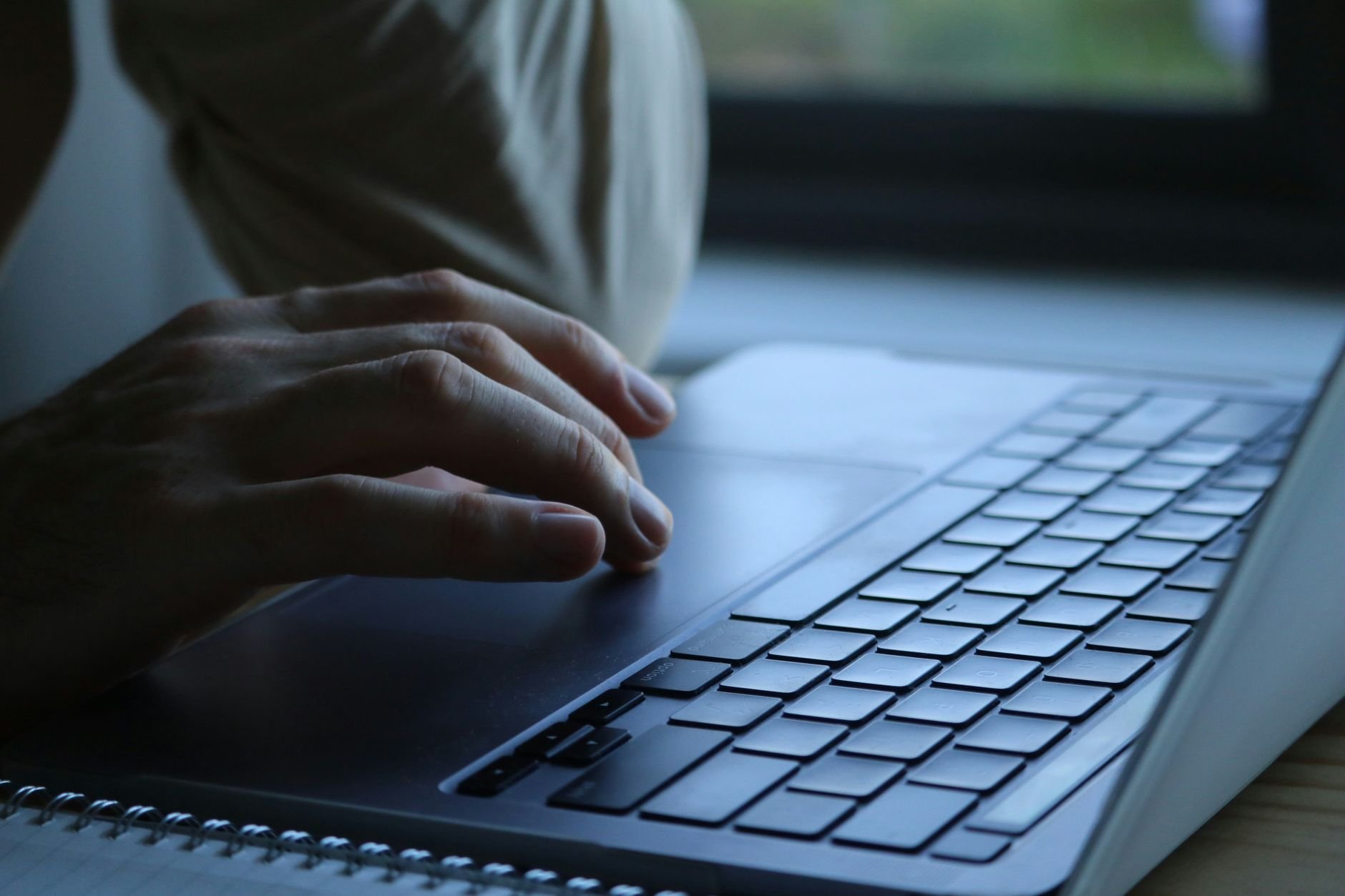 Close-up of a person's hands typing on a laptop keyboard indoors. Soft lighting.
