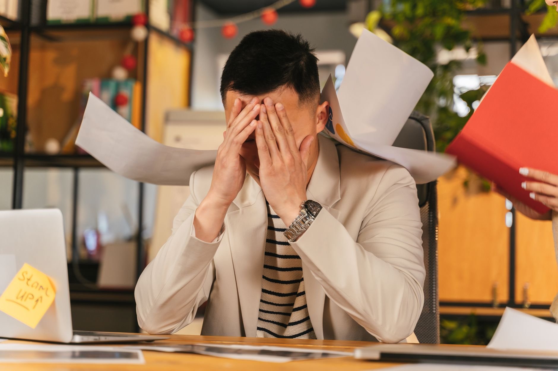 Stressed business owner overwhelmed by paperwork in an office environment.